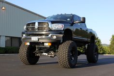 a large black truck is parked in front of a building with huge tires on it