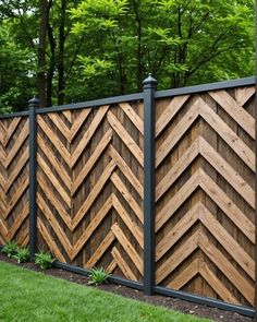 a wooden fence with black metal posts and wood chevrons on the sides, in front of some trees