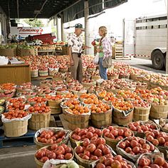 people shopping at an outdoor farmers market with lots of tomatoes and other fruits in baskets