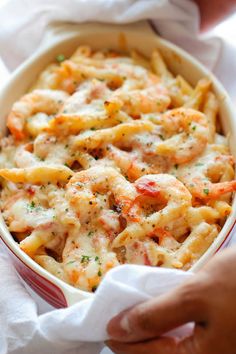 a person is holding a dish full of pasta and shrimp in a casserole