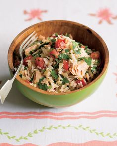 a green bowl filled with rice and vegetables on top of a white table cloth next to a fork