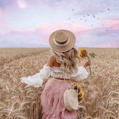 a woman in a pink dress and straw hat walking through a field with a sunflower