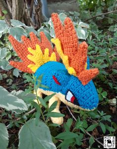 a crocheted stuffed animal head laying in the grass next to some leaves and plants