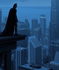 a batman standing on top of a tall building with city lights in the back ground