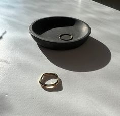 a black bowl sitting on top of a white table next to a gold wedding band