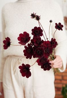 a woman holding a bunch of flowers in her hands and wearing a white sweater over it