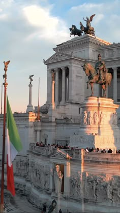 there is a statue on top of the building with flags flying in front of it