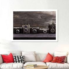 three old cameras sitting on top of a white couch in front of a wooden wall