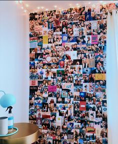 a wall covered in pictures and lights next to a table with a lamp on it