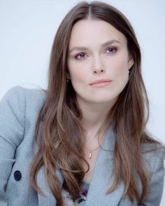 a woman with long brown hair wearing a gray blazer and white shirt is looking at the camera