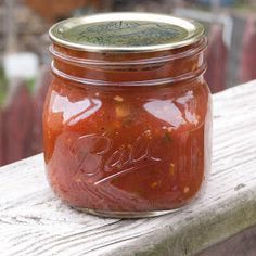 a jar of tomato sauce sitting on top of a wooden table next to a fence