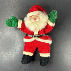 a small stuffed santa clause doll with green arms and legs on a gray surface,