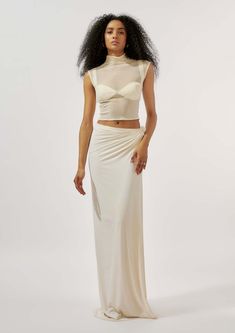 Emanate elegance and contemporary allure with this ensemble comprising a malai lycra draped skirt featuring intricately crafted knot detailing at the waist. Paired harmoniously with a modal satin pleated bralette, exuding sophistication and a touch of luxury. Complete the look with a mesh high neck top, adding a modern twist and ensuring you stand out with refined confidence at any upscale event or stylish gathering. Elegant Fitted Sheer Crop Top, Elegant Sheer Crop Top For Evening, Elegant Sheer Evening Crop Top, Fitted White Draped Skirt For Summer, Elegant Sheer Crop Top For Night Out, Elegant Cream Crop Top, Sheer Fitted Crop Top For Evening, White Fitted Draped Skirt For Party, Elegant Ruched Sleeveless Crop Top