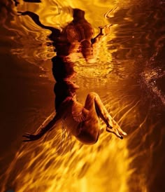 a woman floating in the water on top of a body of water with fire behind her