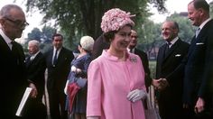 a woman in a pink dress and white gloves shaking hands with other people