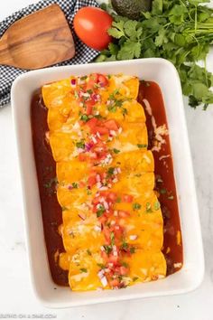 an enchilada in a white casserole dish with tomatoes and parsley on the side