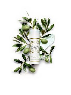 an image of some olives and leaves on a white background with a bottle of lotion next to it