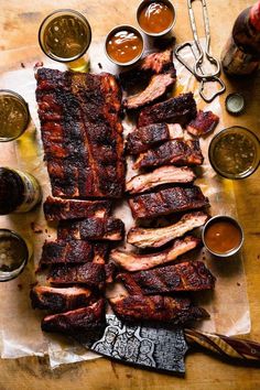 barbecue ribs and sauces on a cutting board with utensils next to them