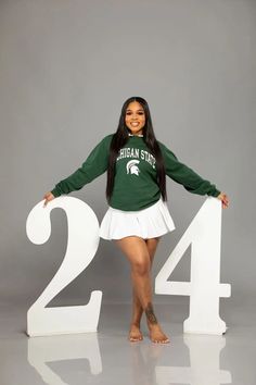 a woman in a green shirt and white skirt standing next to the number twenty four