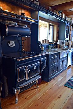 an old fashioned stove is in the middle of a wood floored kitchen with black cabinets