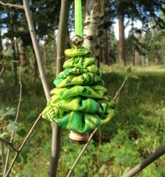 a green christmas tree ornament hanging from a tree in a forest with grass and trees behind it