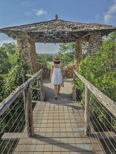 a woman in a white dress and hat walks across a bridge with a gazebo