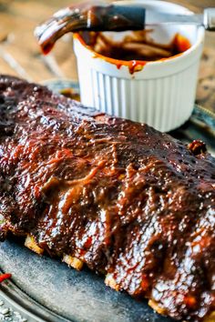 ribs covered in bbq sauce on a plate next to a bowl of barbecue sauce