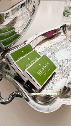 two silver trays with green business cards on them sitting next to each other in front of a mirror