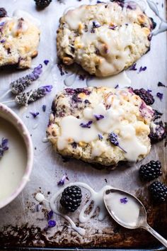 blackberry cookies with white icing and blackberries on a baking sheet next to a bowl of yogurt