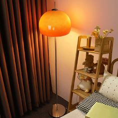 an orange floor lamp sitting on top of a wooden shelf next to a bed in a bedroom