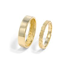 two gold wedding bands with engraved designs on the sides, one in yellow gold and the other in white gold