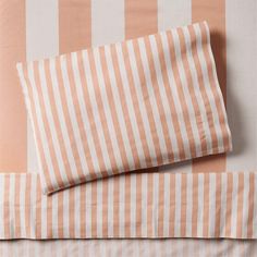 an orange and white striped sheet set on top of a bed with two pillow cases