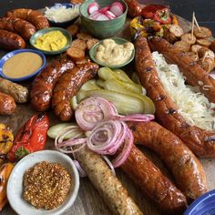 an assortment of meats and vegetables on a cutting board with dipping sauces in bowls