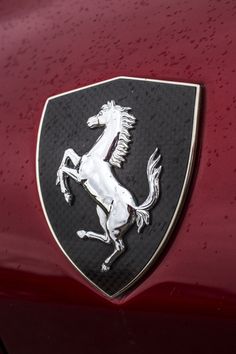 the front end of a red car with a black and silver horse on it's emblem