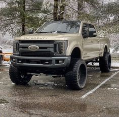 a white truck parked in a parking lot next to some trees and snow covered ground