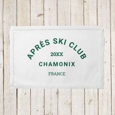 a white towel with the words apres ski club in green lettering on it, hanging from a wooden wall