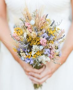 a woman in a white dress holding a bouquet of wildflowers and grasses with her hands