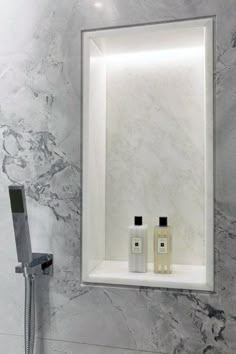 a bathroom with marble walls and flooring, two bottles of cologne on the shelf