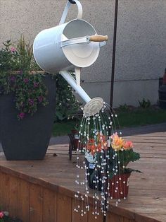 a metal watering can with flowers hanging from it's side on a wooden deck