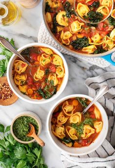 two bowls of pasta and spinach soup on a marble counter top with spoons