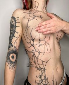 a woman with tattoos on her back holding her hand up to her chest and looking at the camera