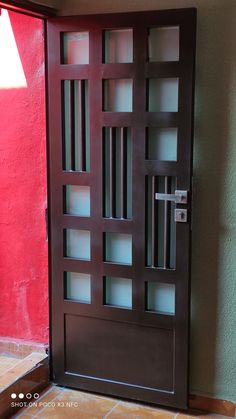 a wooden door with glass panels and a lamp on the side walk in front of a red wall