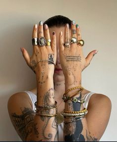 a woman with tattoos covering her eyes and holding her hands up to her face while wearing multiple rings