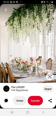 an image of a table setting with flowers and greenery hanging from it's ceiling