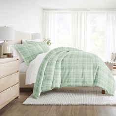 a green and white plaid comforter set on a bed in front of a window