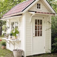 a small white shed sitting in the middle of a yard with potted plants on it