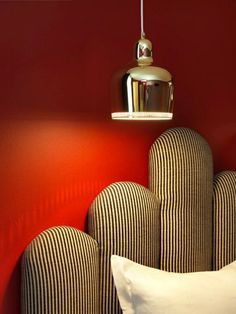 a bed with pillows and a lamp hanging from the headboard in a red room