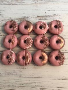 pink donuts with gold sprinkles are arranged on a white wooden surface