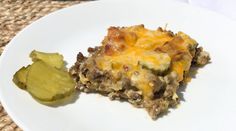 a white plate topped with a casserole covered in cheese and meat next to a pickle