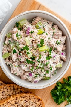 a white bowl filled with tuna salad on top of a cutting board next to bread